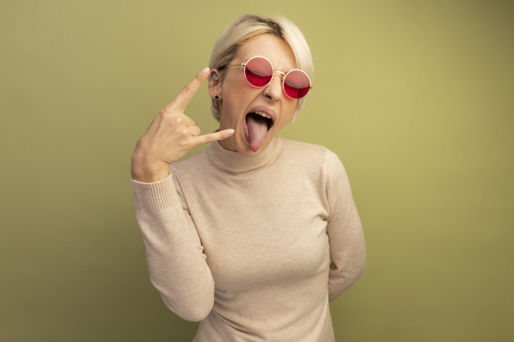Uśmiechnięta kobieta pokazuje język i wykonuje gest dłoni. Zdjęcie ilustrujące różnorodne opinie i emocje towarzyszące dyskusjom o starzeniu się w Internecie.